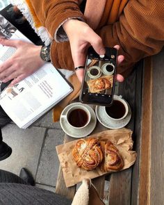 two people sitting at a table with coffee and pastries in front of their cell phones