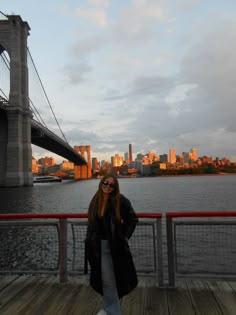 a woman standing in front of a bridge with the cityscape in the background