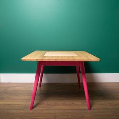 a wooden table with red legs in front of a green wall and wood flooring