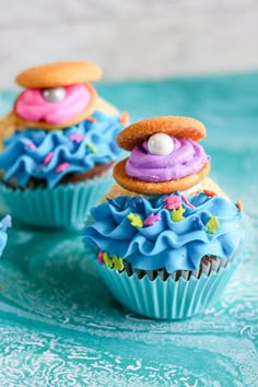 three cupcakes with blue frosting and sprinkles on them sitting on a table