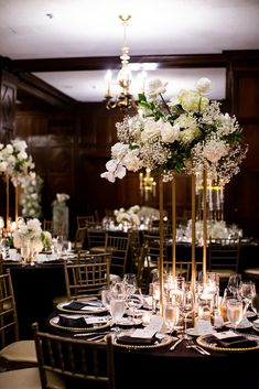 a tall centerpiece with white flowers and greenery sits on top of a round table