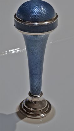 a silver and blue vase sitting on top of a white table next to a wall