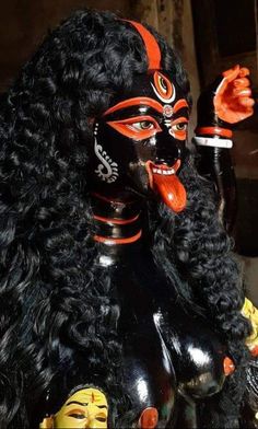 a woman with long black hair and orange face paint on it's face, holding an item in her hand