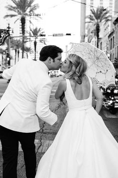 a bride and groom kissing under an umbrella on the sidewalk in front of palm trees