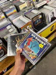 a person holding up a cd case in front of a store shelf filled with cds