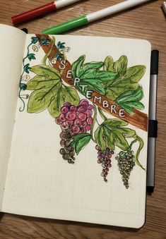 an open notebook with grapes and leaves on the cover, next to two colored markers