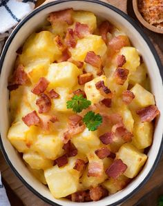 a bowl filled with potatoes and bacon on top of a wooden table