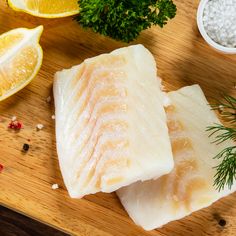 two fish fillets sitting on top of a cutting board next to lemons and spices