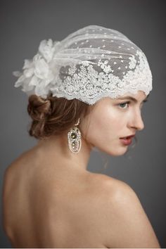 a woman wearing a white veil with flowers on the head and hair in a bun