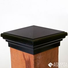 a wooden post with a black top and brown trim around the base is against a white wall