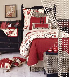 a bedroom with red and white bedding, pillows and blankets on the floor next to a night stand