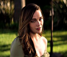 a woman sitting in the grass with an umbrella over her head and looking at the camera