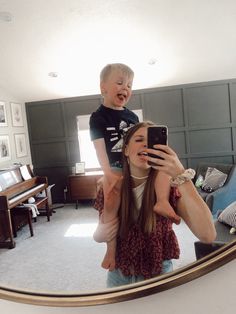 a woman holding a child in front of a mirror with the reflection of another person taking a selfie