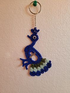 a crocheted keychain hanging on a wall with a blue and green lizard