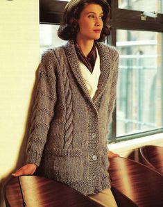 a woman standing next to a window wearing a sweater and jacket