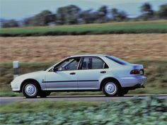 a white car driving down the road in front of a field with crops behind it