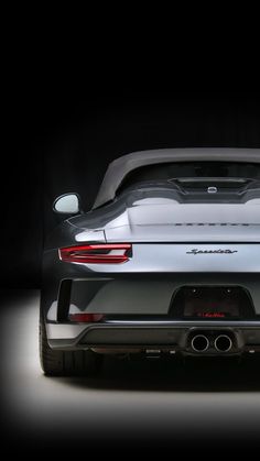 the rear end of a silver porsche sports car in a dark room with its lights on