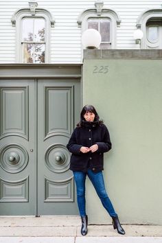 a woman leaning against a wall in front of a building with two doors and a lamppost