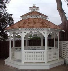 a white gazebo sitting in the middle of a yard next to a fence and tree