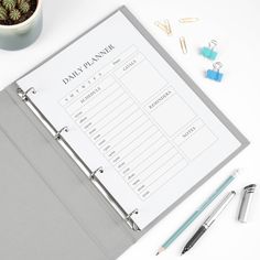 a desk with a planner, pen and office supplies next to it on top of a white surface