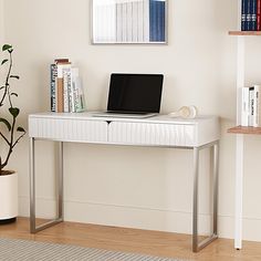 a laptop computer sitting on top of a white desk next to a potted plant