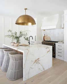 a kitchen with marble counter tops and gold pendant light over the island in front of it