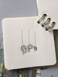 an open notebook with two plants hanging from it's sides, on top of a table