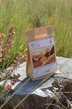 a bag of coffee sitting on top of a tree stump in front of some flowers