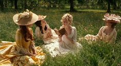 three women sitting in the grass with hats on their heads and one reading a book