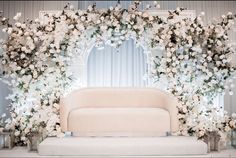 a couch sitting in front of a white flower covered wall with candles and flowers around it