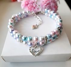 two bracelets with charms and flowers on top of a white box next to pink flowers