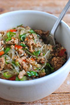 a white bowl filled with meat and vegetables on top of a wooden table next to a spoon