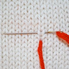 the crochet stitch is being worked on with an orange yarn ball and needles