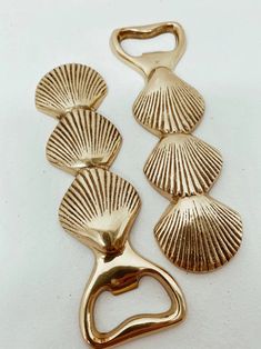 three gold seashells hang on a white surface with a metal hook in the middle