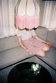 a woman sitting on top of a gray couch next to a table with a flower in it