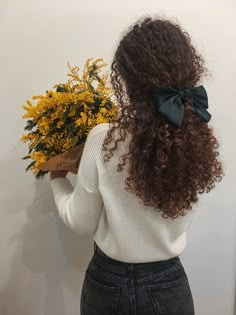 a woman with curly hair wearing a white sweater and black bow tie holding a bouquet of yellow flowers