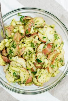 a glass bowl filled with potato salad on top of a white cloth and silver spoon