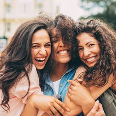 three young women are hugging and smiling together