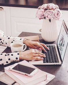 a woman is typing on her laptop while holding a cup of coffee and pink flowers