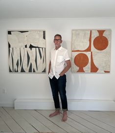 a man standing in front of two paintings on the wall with his hands in his pockets