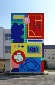 a large building with many different colors and shapes on it's side in front of a parking lot