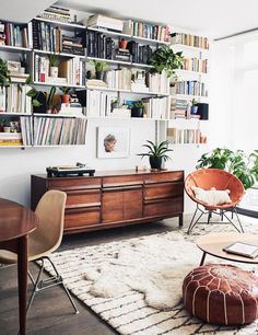 a living room filled with lots of books and furniture next to a wall mounted book shelf