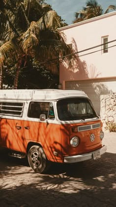 an orange and white vw bus parked in front of a house with palm trees