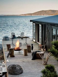 a deck with chairs and fire pit on the water's edge next to a house