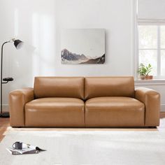 a living room with a brown leather couch and white rugs on the hardwood floor