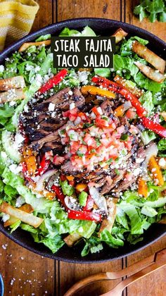 a salad in a black bowl on top of a wooden table next to utensils