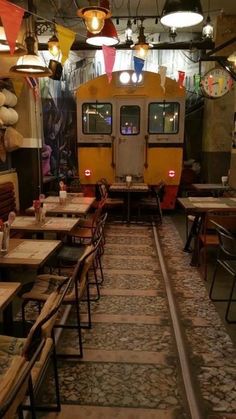 an empty restaurant with tables and chairs in front of a yellow train on the tracks