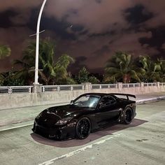 a black sports car is parked on the side of the road at night with palm trees in the background