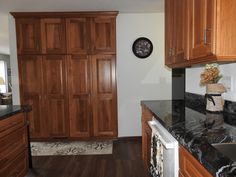 a kitchen with wooden cabinets and marble counter tops, along with a clock on the wall