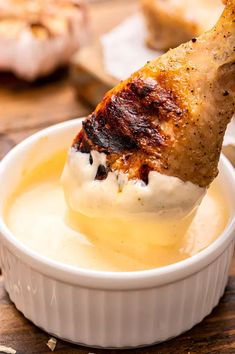 a piece of chicken is being dipped with ranch dressing in a white bowl on a wooden table